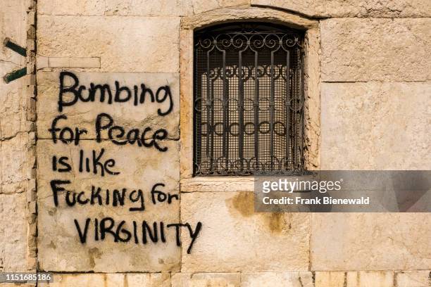 The saying 'Bombing for peace is like fucking for virginity' sprayed as graffity at a house facade.