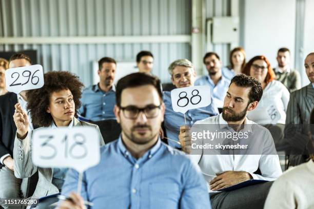 crowd of business people having an auction in a board room. - auction stock pictures, royalty-free photos & images