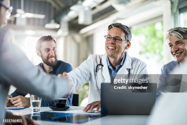 happy doctor shaking hands with a businessman on a meeting in the office. - doctor recruitment stock pictures, royalty-free photos & images