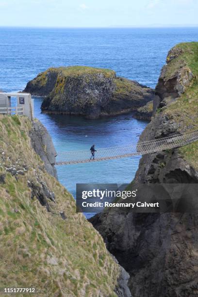 lone woman crossing carrick-a-rede bridge, antrim coast. - northern ireland rope bridge stock-fotos und bilder