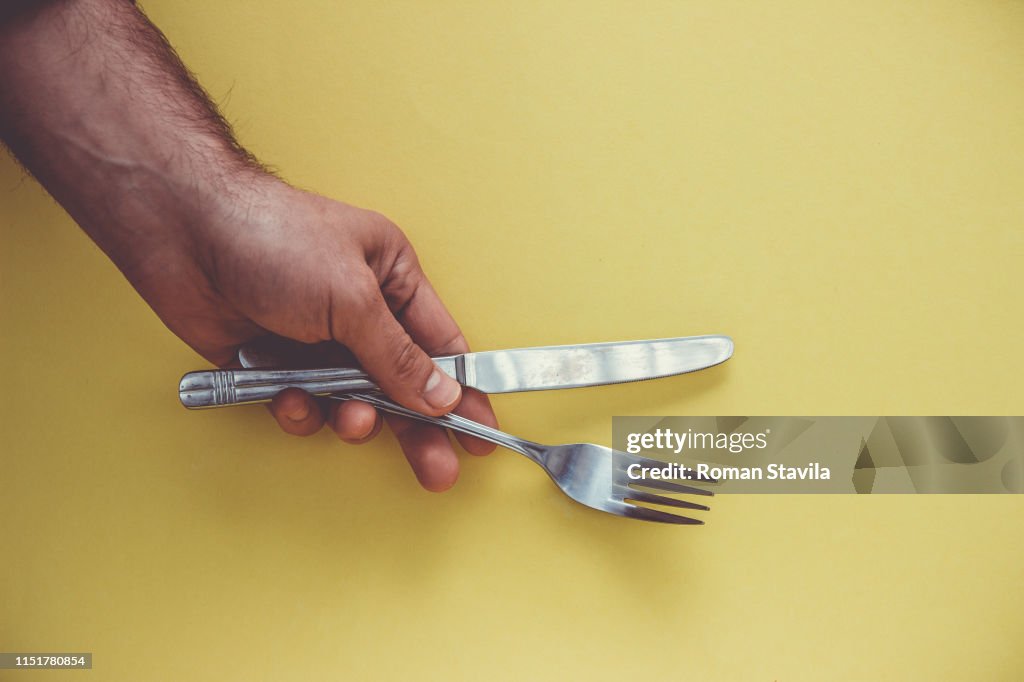 Hand with knife and fork on a yellow background.