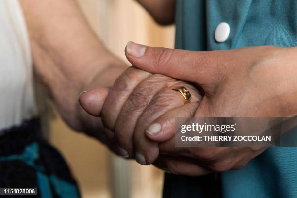 This picture taken on June 25, 2019 in Clermont-Ferrand shows a personal care assistant holding the hand of an elderly person as she visits her house...