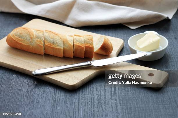 traditional breakfast. bread (sliced baguette) on cutting board with butter on plate on dark background. - baguette white stock pictures, royalty-free photos & images