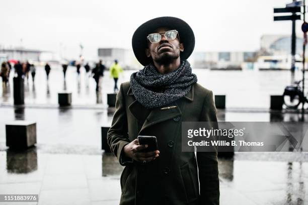 black man looking up while holding smartphone - gray coat stock pictures, royalty-free photos & images