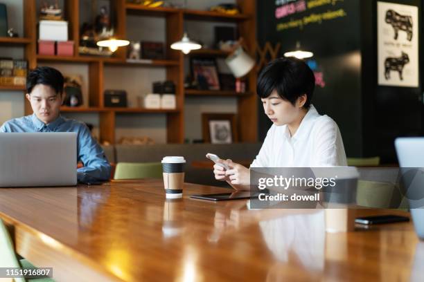 business send text message via mobile phone at office - taiwanese etniciteit stockfoto's en -beelden