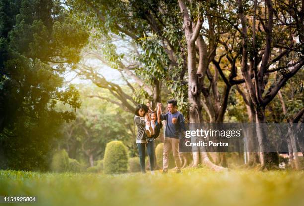 playful parents swinging daughter in public park - family in the park stock pictures, royalty-free photos & images