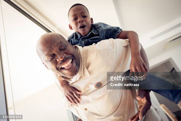 low angle view of grandfather piggybacking boy - piggyback stock pictures, royalty-free photos & images