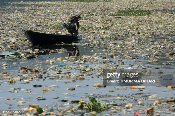 Scavenger paddles his wooden boat to collect plastic waste for recycling on the Citarum river choked with garbage and industrial waste, in Bandung,...