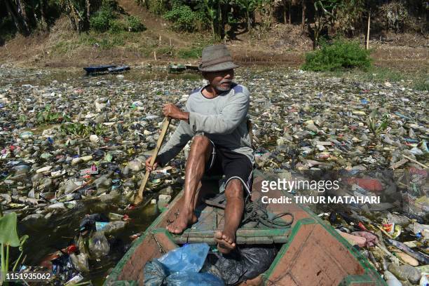 Scavenger paddles his wooden boat to collect plastic waste for recycling on the Citarum river choked with garbage and industrial waste, in Bandung,...