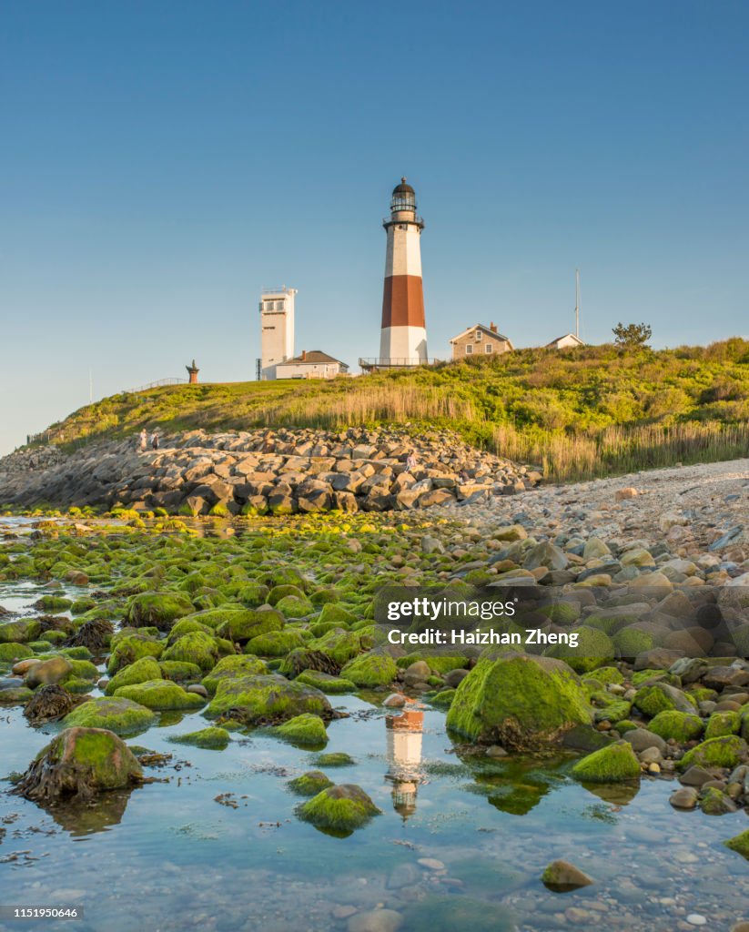 Lighthouse beacon sitting on a cliff overlooking the ocean during sunset.