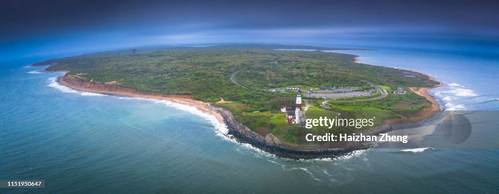 Lighthouse beacon sitting on a cliff overlooking the ocean during sunset.