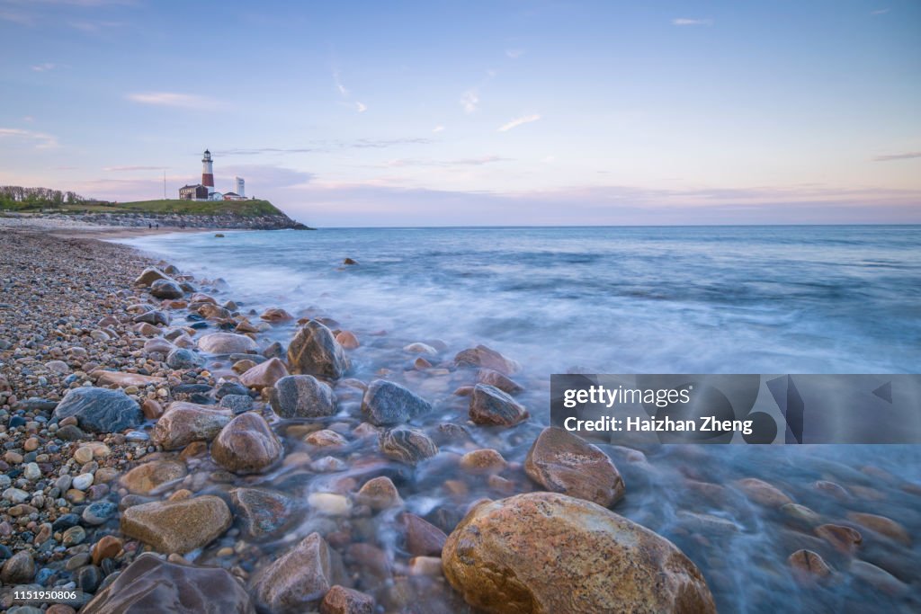 Lighthouse beacon sitting on a cliff overlooking the ocean during sunset.