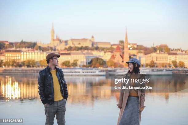 couple standing along danube river with buda castle hill and urban skyline reflection at dawn, budapest, hungary - budapest skyline stock pictures, royalty-free photos & images