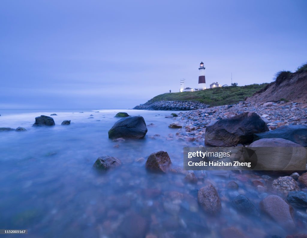 Lighthouse beacon sitting on a cliff overlooking the ocean during sunset.