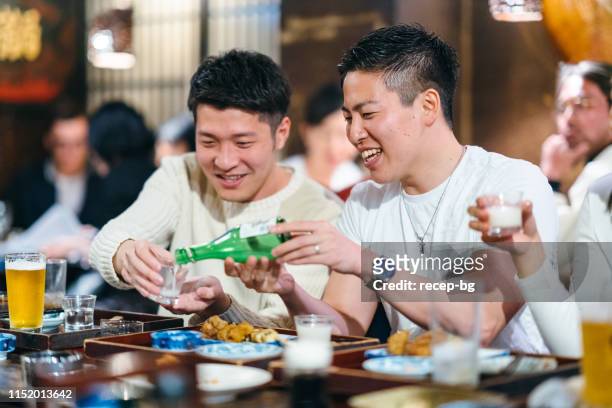 man pouring alcohol to his friend’s cup - sake stock pictures, royalty-free photos & images