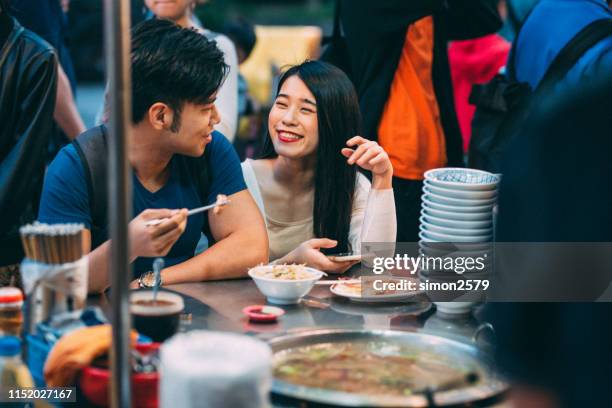 lovely young asian couple enjoying street food in night market, taipei. - night market stock pictures, royalty-free photos & images