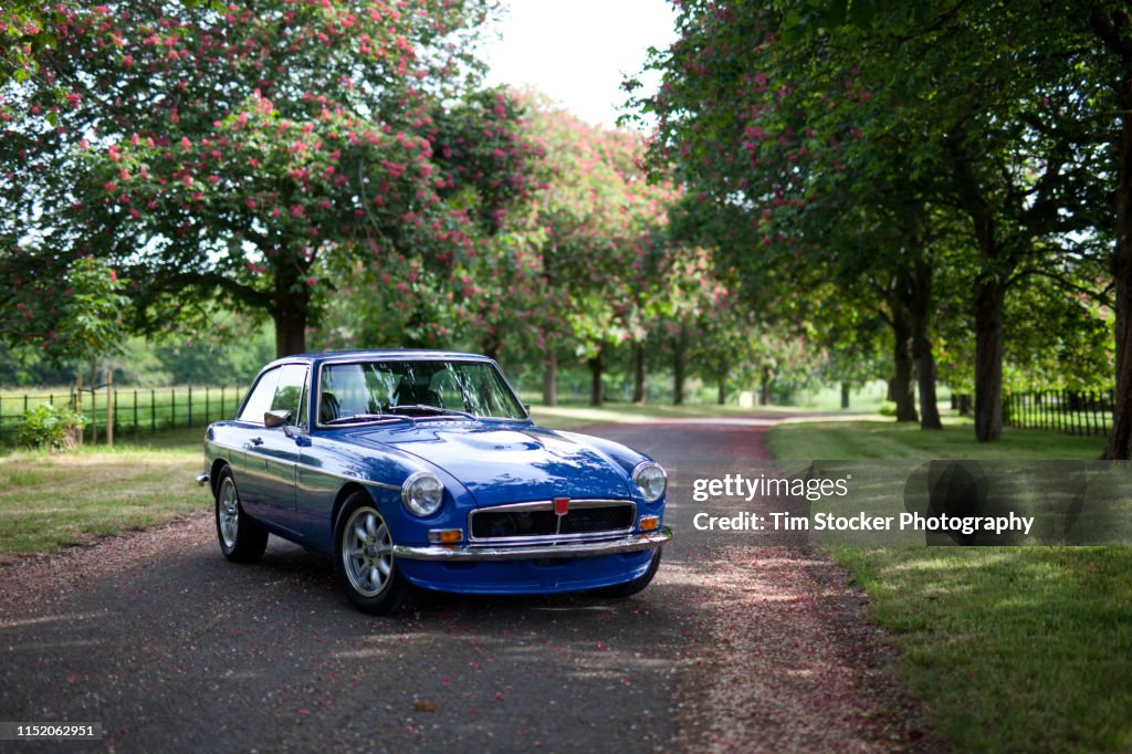 A blue classic car parked on a pretty leafy lane, in Horsham, West Sussex, UK.