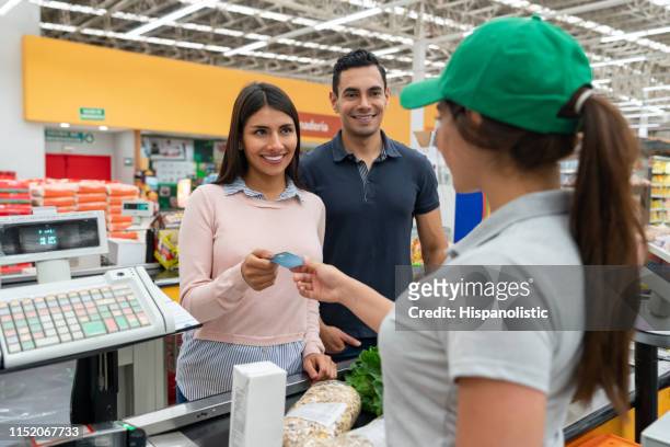 bellissimo cliente di coppia che paga per la spesa al registratore di cassa con carta di credito sorridente - paying supermarket foto e immagini stock