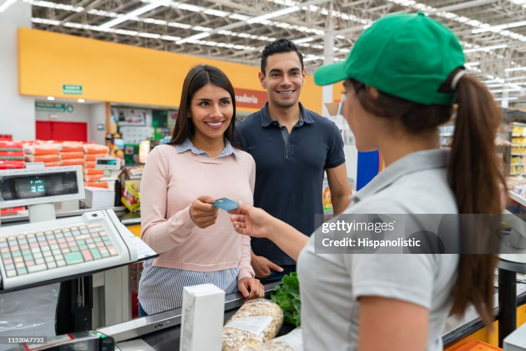 Beautiful couple customer paying for groceries at the cash register with credit card smiling