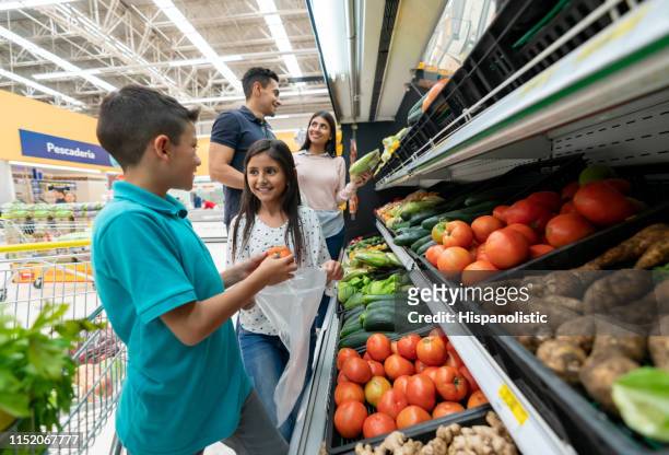 latinamerikansk familj i stormarknaden shopping för grönsaker medan du pratar och har roligt - latin american and hispanic shopping bags bildbanksfoton och bilder