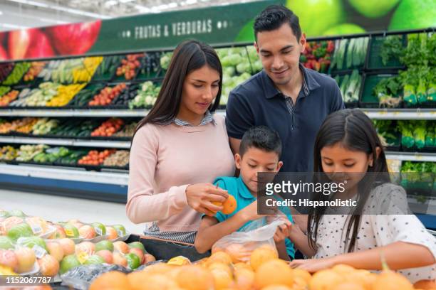 glad latinamerikansk familj på stormarknaden shopping för frukter medan du pratar - latin american and hispanic shopping bags bildbanksfoton och bilder