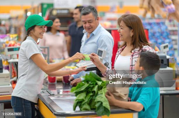 latin american mother and son paying for groceries at the supermarket while other customers wait in line - supermarket queue stock pictures, royalty-free photos & images