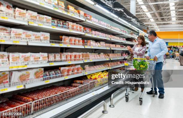 mature woman showing partner label on refrigerated product at the grocery store - pork sausage stock pictures, royalty-free photos & images
