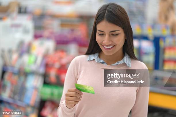 young woman looking at a loyalty card from supermarket smiling - loyalty cards stock pictures, royalty-free photos & images