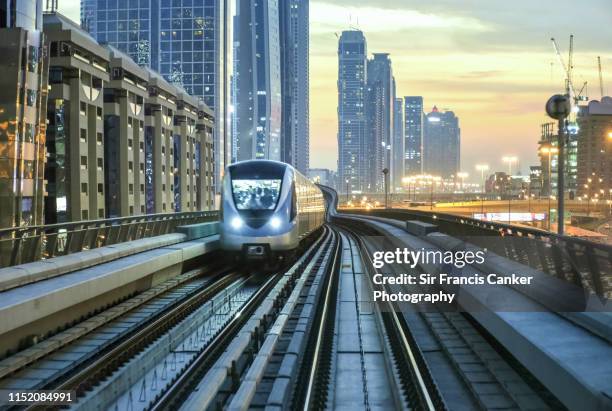 dubai skyline illuminated at sunset with driverless metro train approaching fast, uae - train vehicle stock-fotos und bilder