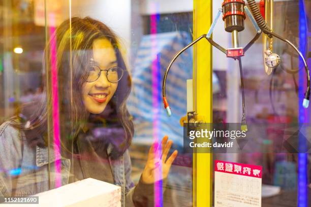 young asian woman playing the claw game in an arcade - claw machine stock pictures, royalty-free photos & images