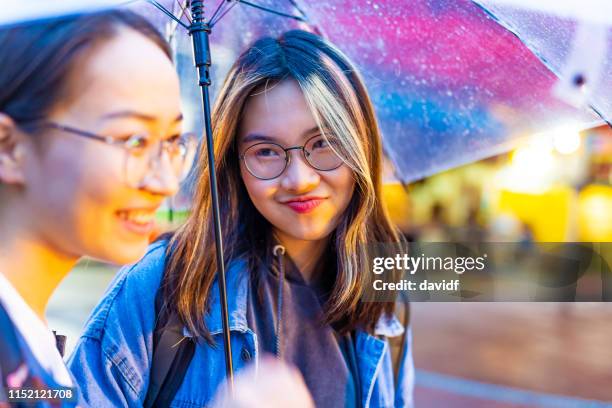 smiling happy asian women enjoying a night out shopping in the rain - girl rain night stock pictures, royalty-free photos & images