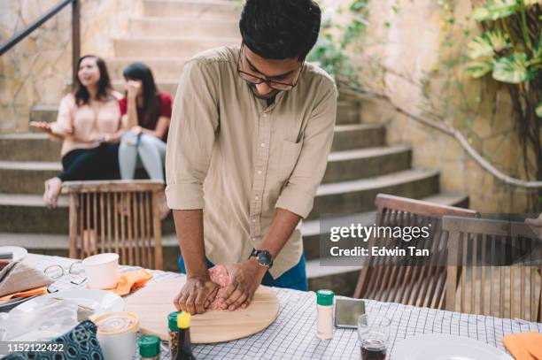 an asian male preparing food at the outdoor kitchen while his friends behind chatting - moving toward stock pictures, royalty-free photos & images