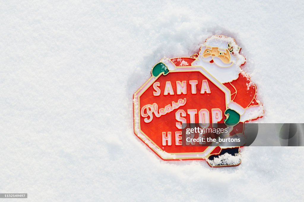 High angle view of "Santa please stop here" sign lies in the snow