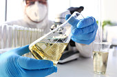 Scientist arm in protective gloves hold yellow liquid in bottle