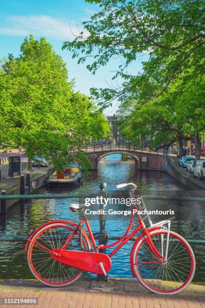 red bicycle on a bridge in amsterdam, the netherlands - amsterdam bike stock-fotos und bilder