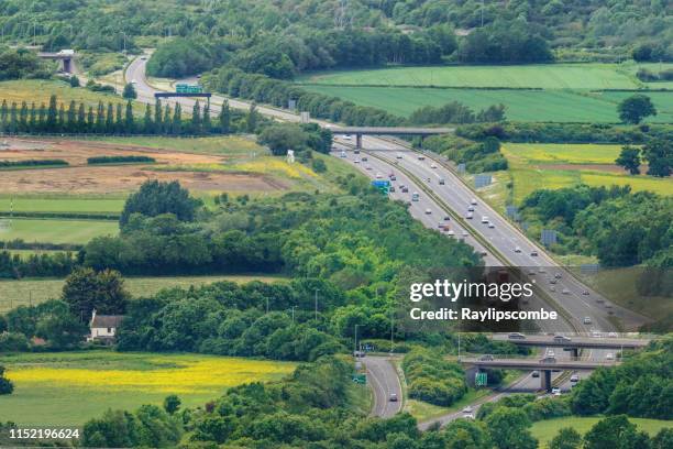 dramatic view over the cotswold landscape showing the busy a417 dual carriageway heading towards gloucester and the m5 junction 11a carving its way through the cotswold landscape - gloucestershire stock pictures, royalty-free photos & images
