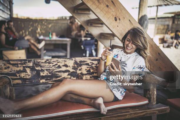 gelukkige vrouw met behulp van mobiele telefoon tijdens het drinken van sap in beach bar. - strandvakantie stockfoto's en -beelden