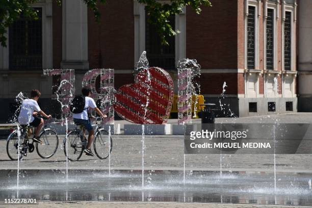 People cycle by a fountain as they cross the Piazza della Vittoria on June 27, 2019 in Reggio Emilia, near Bologna, northern Italy. - Europeans...