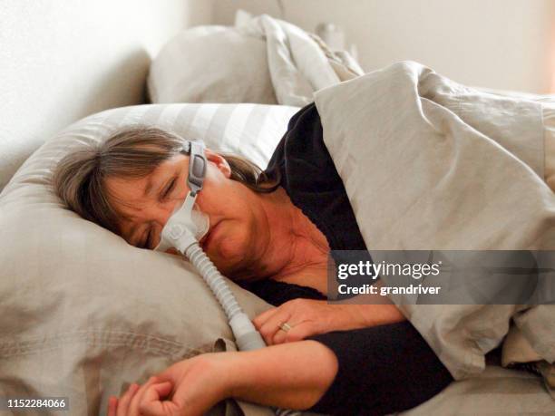 mujer de mediana edad con apnea del sueño durmiendo en una cama con una máquina cpap (presión positiva continua en las vías respiratorias) para ayudar en su sueño - ventilador equipo respiratorio fotografías e imágenes de stock