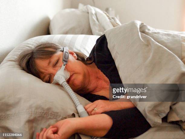 donna di mezza età con apnea del sonno addormentata in un letto indossare una macchina cpap (continuous positive airway pressure) per aiutare a dormire - maschera per l'ossigeno foto e immagini stock