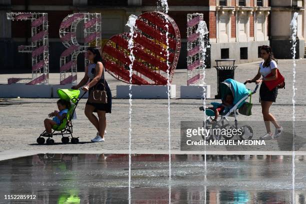 Women pushing toddlers in prams walk by a fountain as they cross the Piazza della Vittoria on June 27, 2019 in Reggio Emilia, near Bologna, northern...