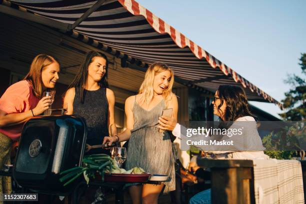 smiling woman showing mobile phone to friends grilling food on barbecue - awning stock pictures, royalty-free photos & images