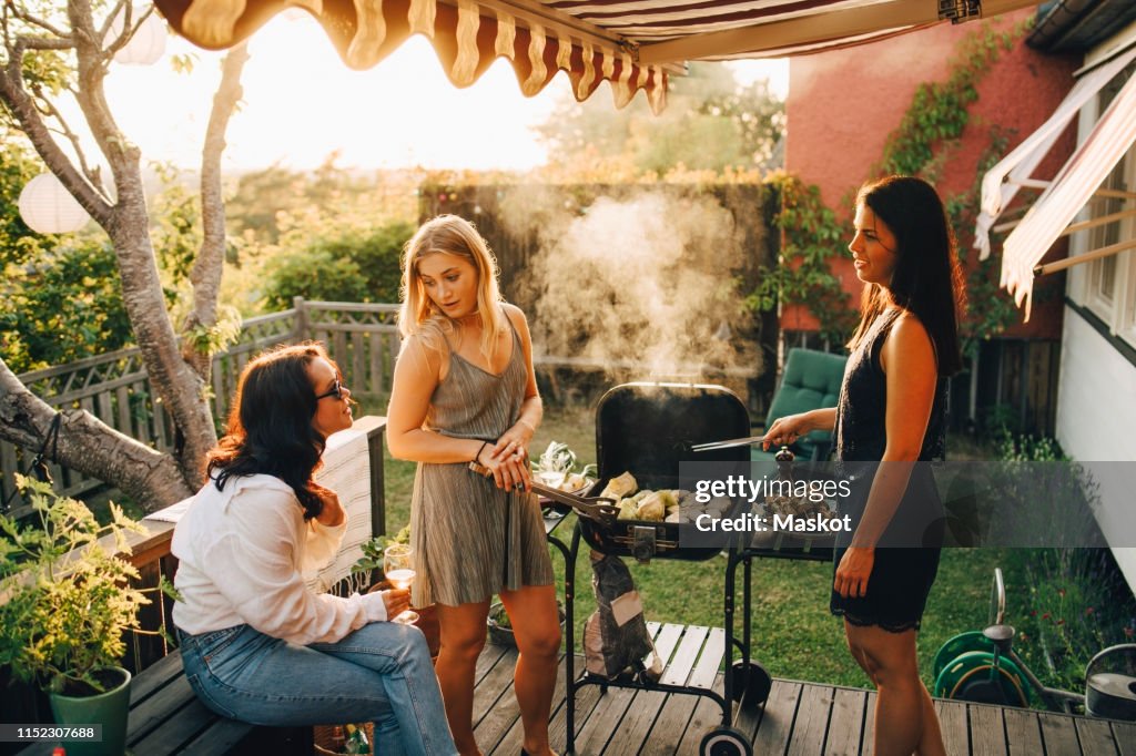 Friends talking while grilling food on barbecue for dinner party in yard