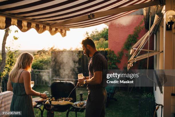 male and female friends grilling food while having wine in party - awning stock pictures, royalty-free photos & images