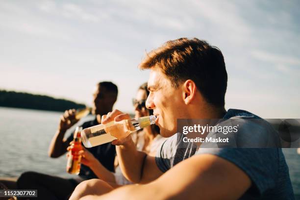 man enjoying drink with friends while sitting on jetty against sky in summer - flat water bottle stock pictures, royalty-free photos & images