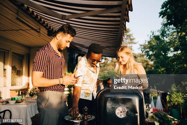 friends talking while enjoying grilled food at dinner party in back yard - backyard barbeque stockfoto's en -beelden