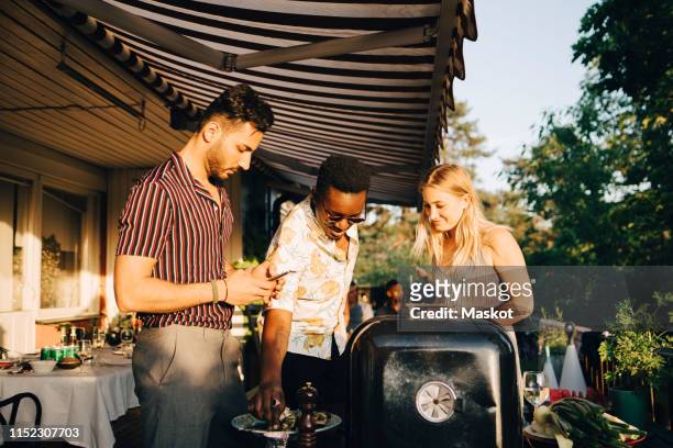 friends talking while enjoying grilled food at dinner party in back yard - backyard barbeque stock pictures, royalty-free photos & images