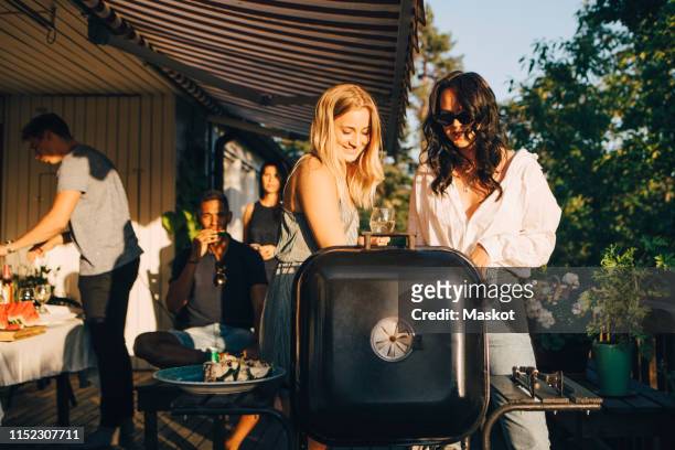 female friends talking while grilling food on barbecue in dinner party - gegrillt stock-fotos und bilder