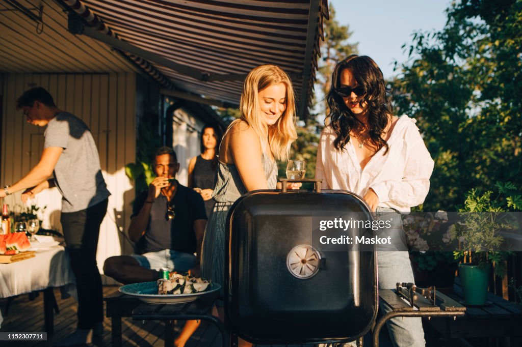Female friends talking while grilling food on barbecue in dinner party