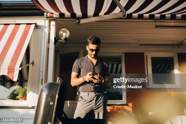 man using smart phone while standing at back yard on sunny day - awning stock pictures, royalty-free photos & images